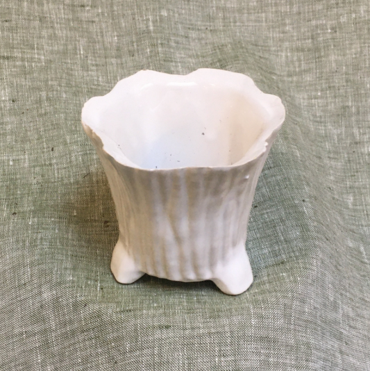 White ceramic pot shaped like a tree trunk with small feet.